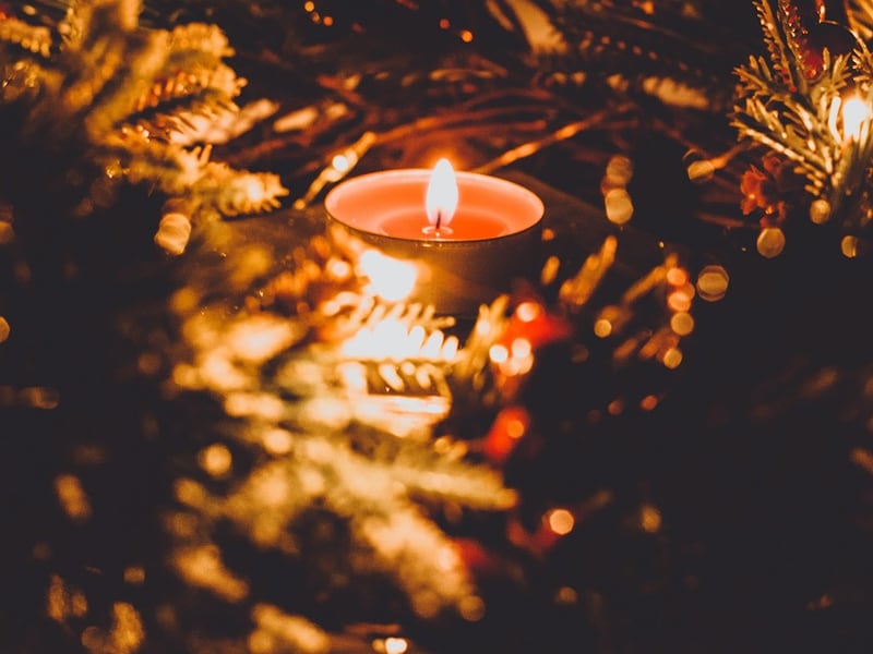 A candle glowing among blurred Christmas tree lights