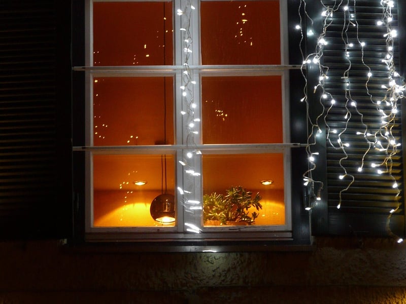 Fairy lights hanging like a curtain beside a warmly lit window at night